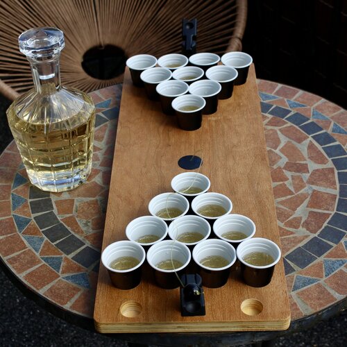 Das Shot Pong Set steht auf einem Tisch mit gefüllten Bechern und einer edlen Glaskaraffe daneben